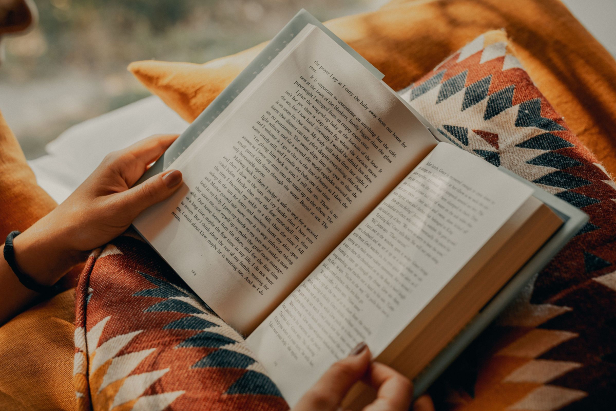 a book is open on a person's lap; they are sitting on colorful cushions